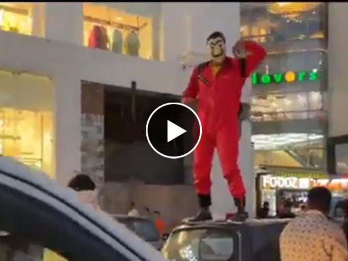 video person throws currency notes on jaipur street on lines of netflix web series money heist | Video - Money Heist स्टाइल मास्क लावलेल्या तरुणाने कारवर चढून उधळल्या नोटा अन्...