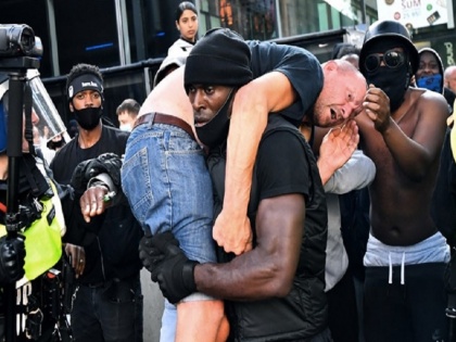 Black Man Carrying Injured White Man At London Protests picture goes viral | काले नागरिक ने नस्लवाद विरोध प्रदर्शन के बीच घायल गोरे शख्स को कंधे पर उठाया, लंदन की तस्वीर सोशल मीडिया पर वायरल